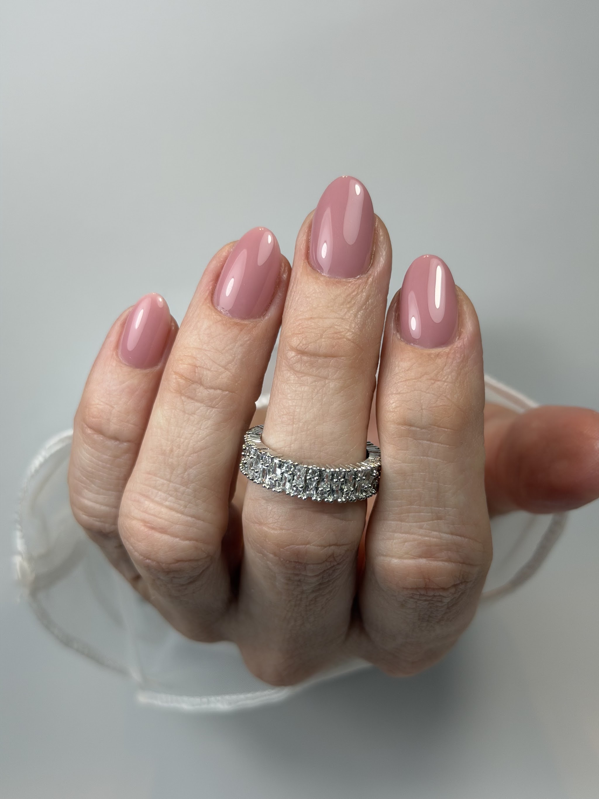 Glanzende oudroze nagels in amandelvorm, met een brede ring met steentjes