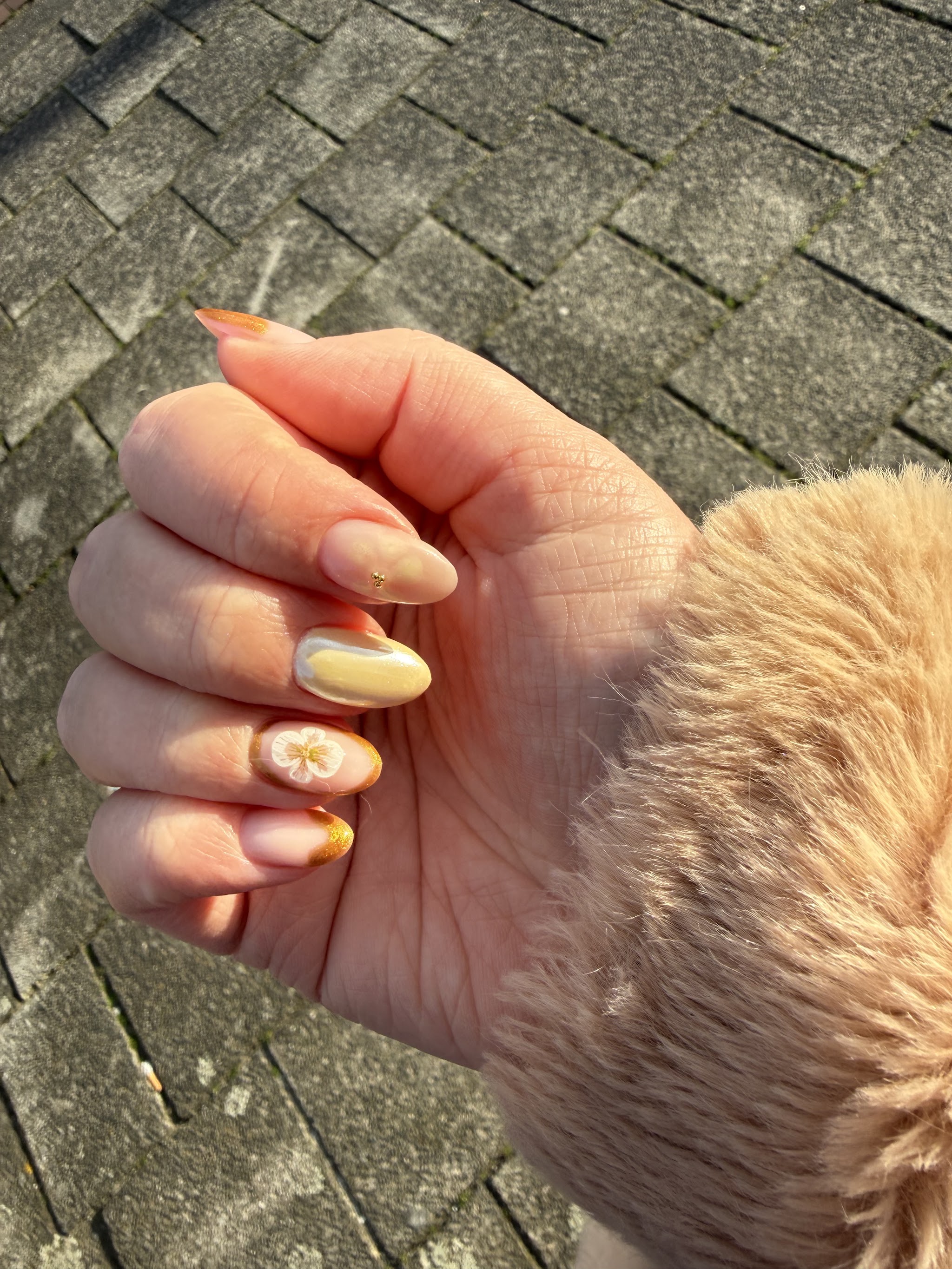 Gele nagels met een bloemetje op twee vingers, buiten in de zon